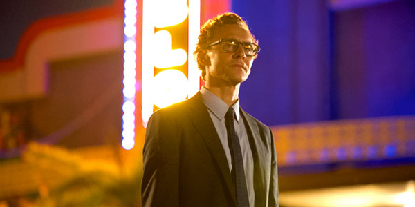 Young white man wearing glasses and a suit in front of a movie theater