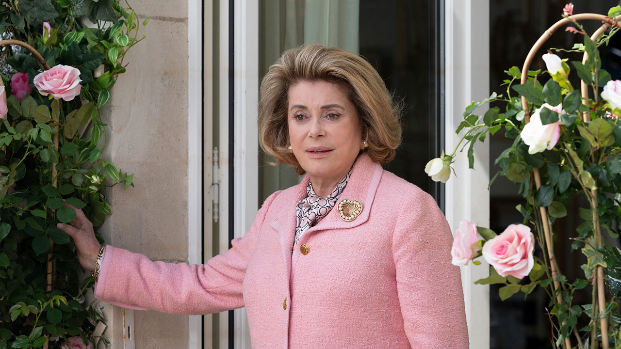 Older woman wearing pink tweed suit standing by flowers