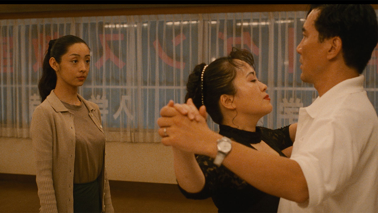 Asian couple ballroom dancing in casual clothing while younger Asian woman watches them