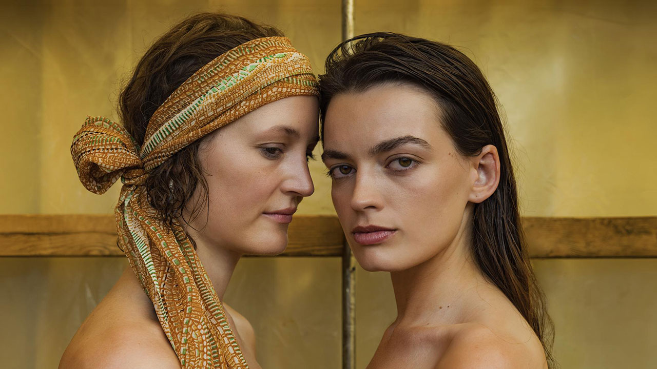 Two women facing each other with a yellow background