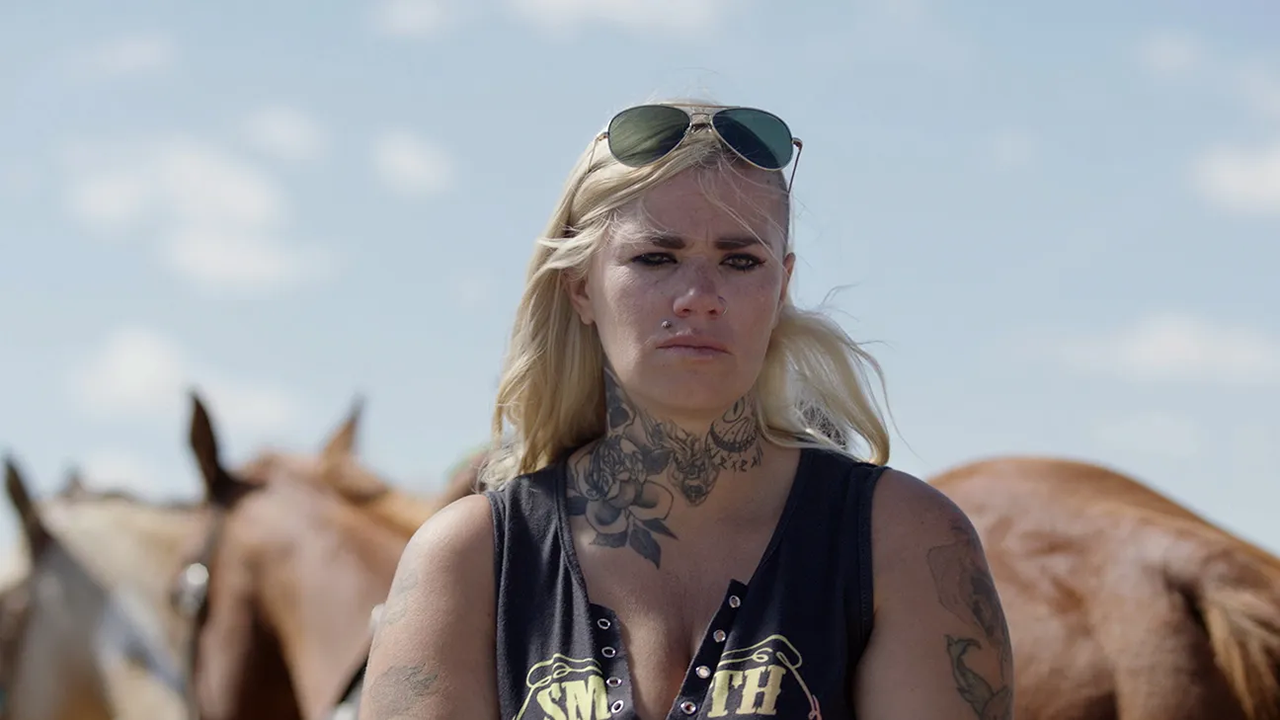 Young blonde woman with tattoos and sunglasses in front of horses