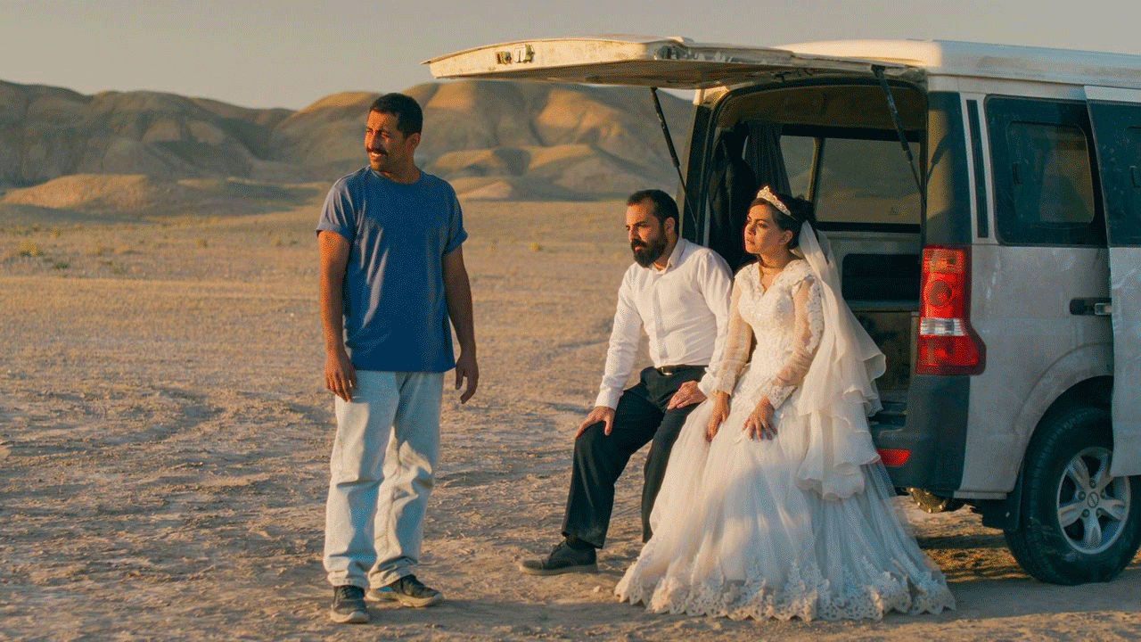 Two Middle Eastern men and a woman in a western wedding dress by a van in the open desert
