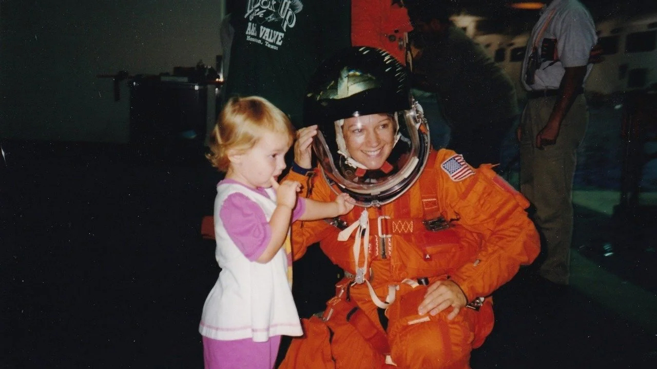 Woman in astronaut suit posing next to young child
