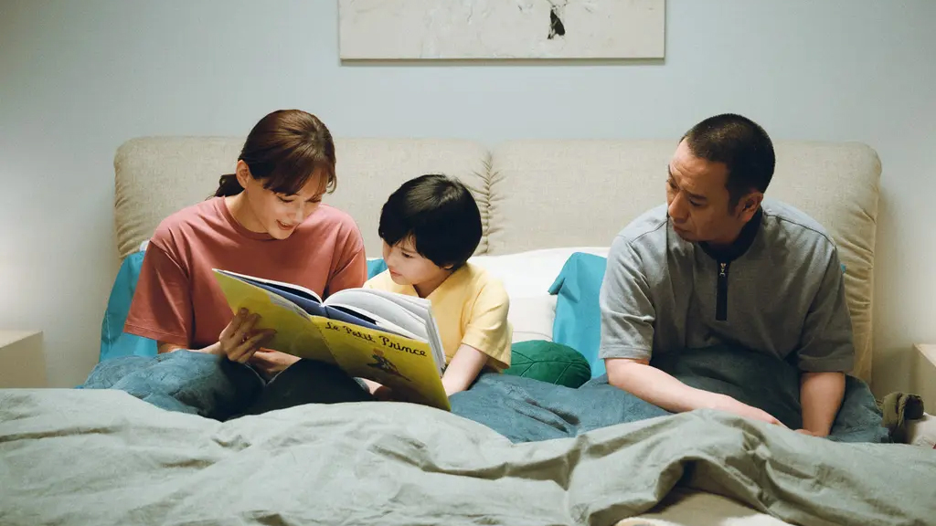 Asian parents sitting in bed reading a book to a young boy