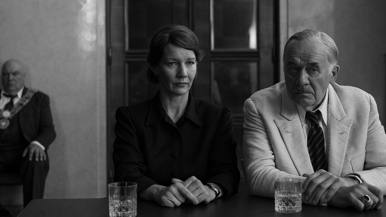 Young white woman wearing a black dress sitting next to her father in white suit