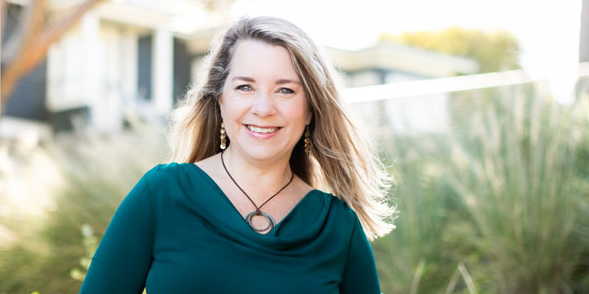 Middle aged blonde woman smiling in teal long sleeve top and black necklace